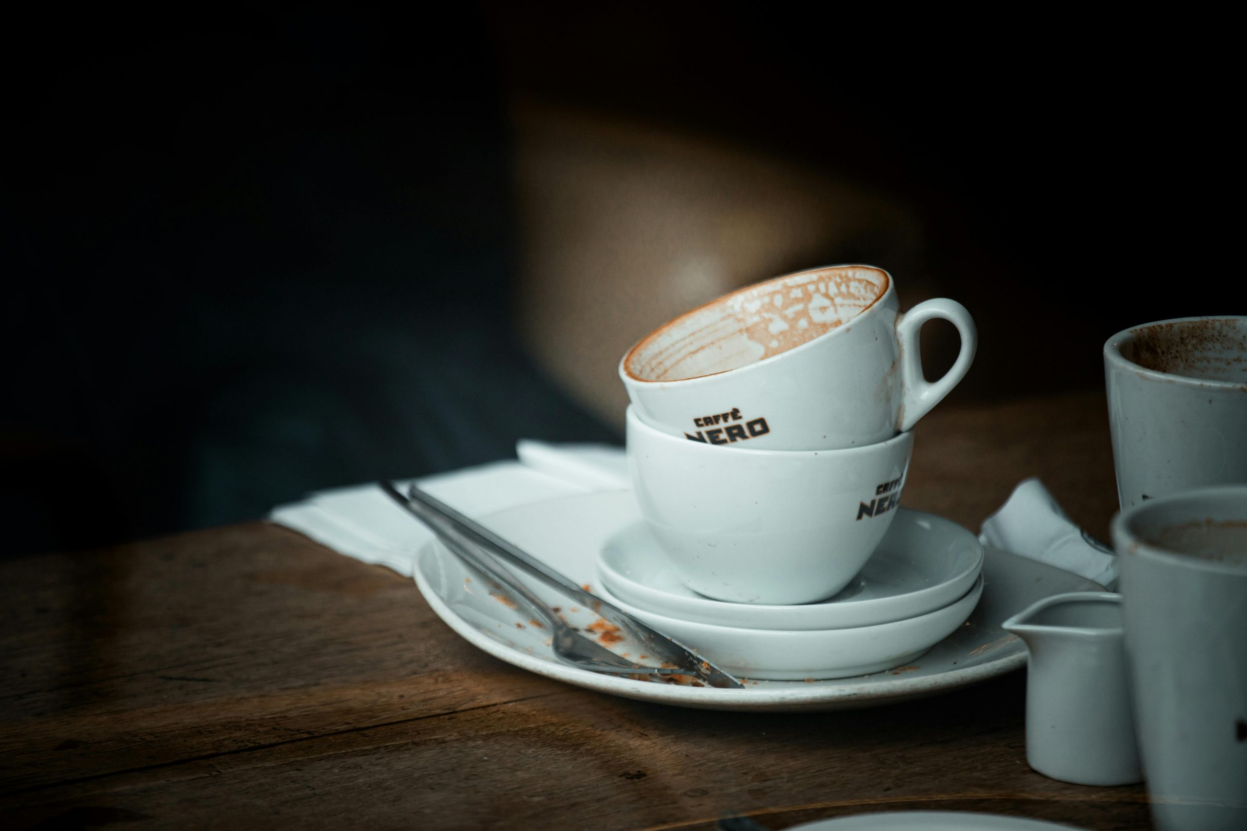 Stacked ceramic coffee cups on a wooden table in a cozy café setting, highlighting vintage café culture.