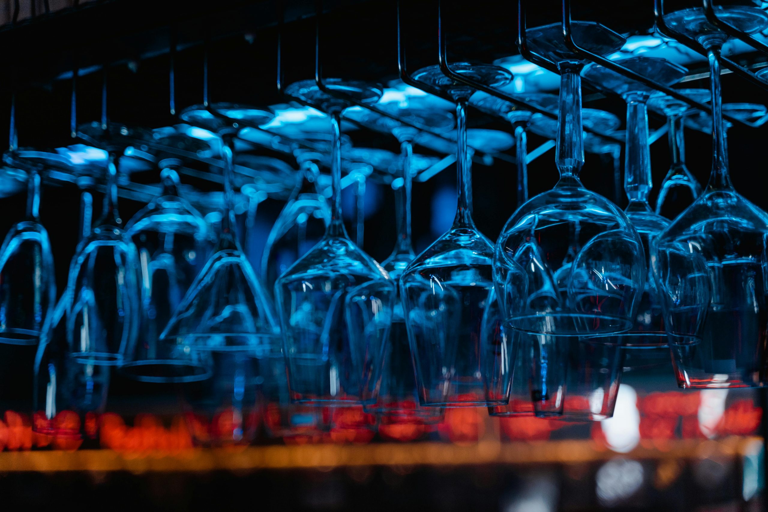 Close-up of glassware hanging upside down inside a bar, illuminated with blue light.